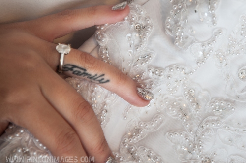 Detail photograph of a brides hand with a tattoo that says "Family" on her ring finger. Her ring finger also has a solitaire diamond engagement ring on it. Her hand is resting on her beaded white wedding dress. Wedding photographer puerto rico.